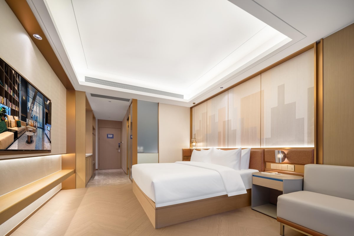 A modern hotel room with a large bed, a seating area, and a TV displaying a cityscape.