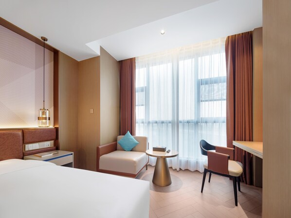 A modern hotel room with a bed, a seating area with a table, and a large window with curtains. - Madison Hotel Wuxi Luocheng (Wuxi)