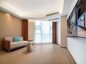 Una habitación de hotel moderna con sofá, una mesita redonda y un ventanal con cortinas.