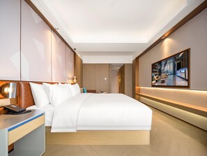 Une chambre d’hôtel moderne dotée d’un grand lit, d’une table de chevet avec un téléphone, d’un téléviseur fixé au mur et d’un couloir menant à une autre chambre.