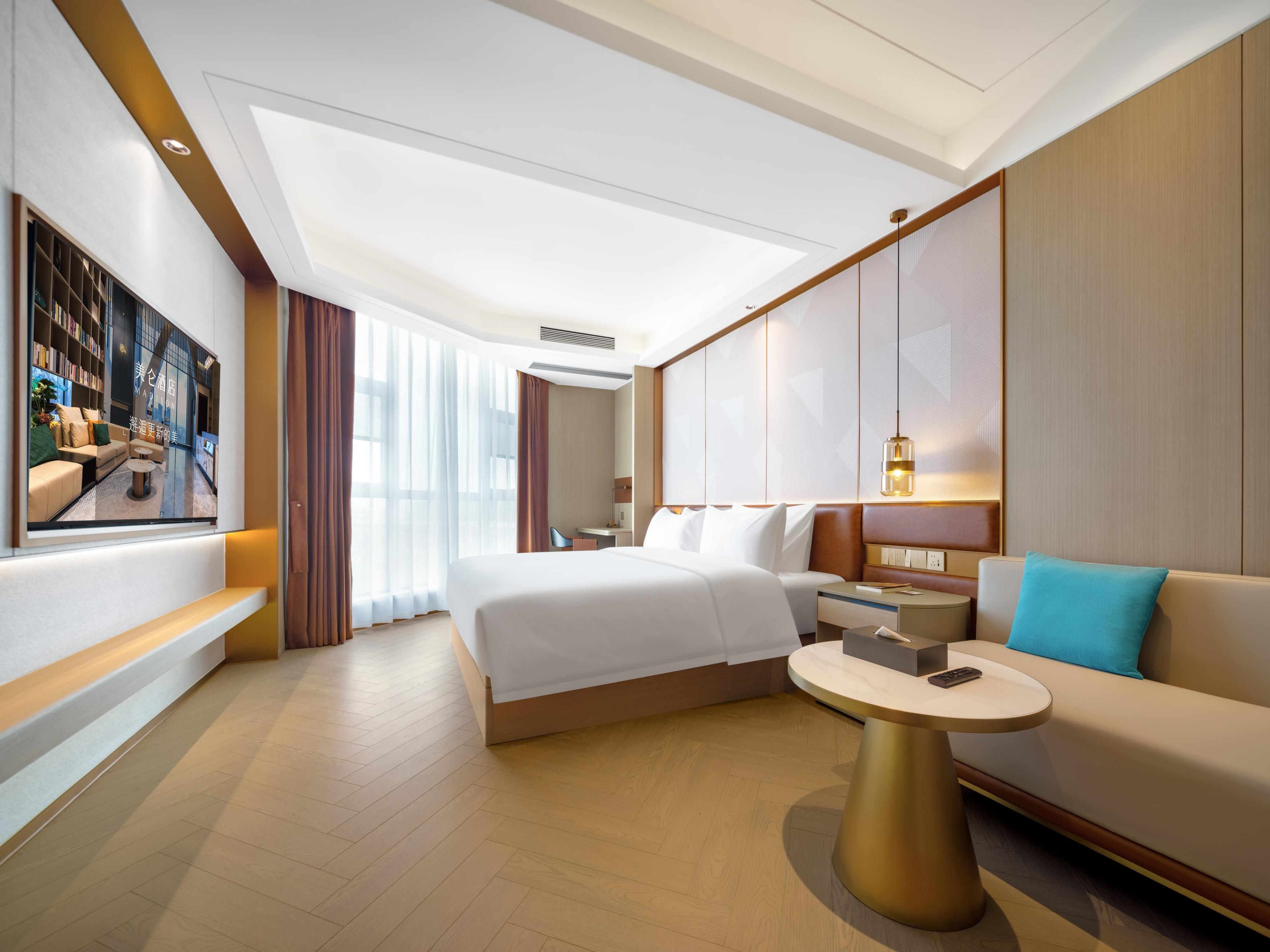 A modern hotel room with a large bed, a sofa, a small round table, and a TV mounted on the wall.
