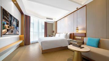 A modern hotel room with a large bed, a sofa, a small round table, and a TV mounted on the wall.