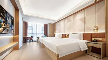 A modern hotel room with a large bed, a desk, and a seating area with a view of the city.