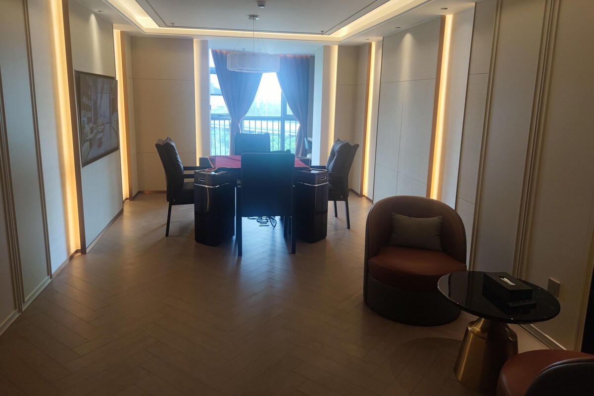 A modern hotel room with a dining area, a sofa, and a small table with a remote control.