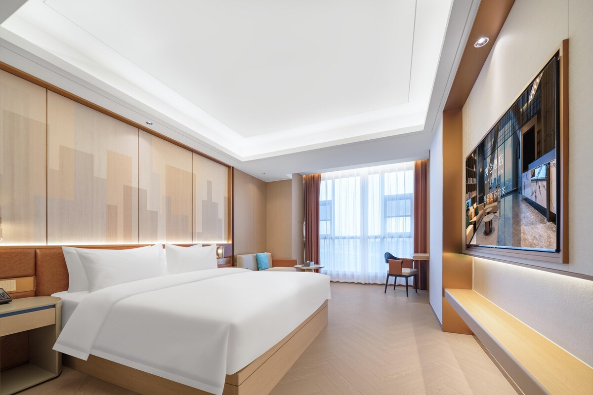 A modern hotel room with a large bed, a desk, and a seating area.