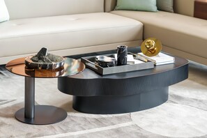 Una sala moderna con una mesa de centro negra, una mesita auxiliar y un sofá.