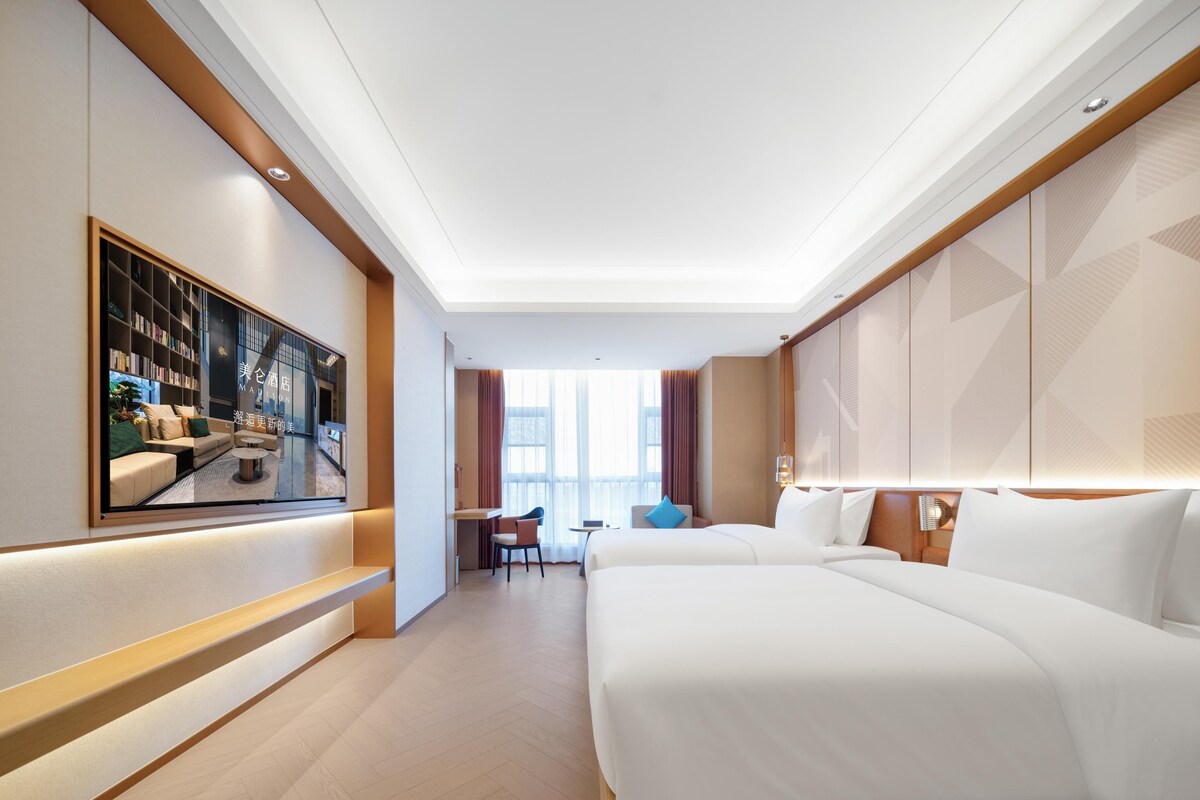 Une chambre d’hôtel avec un grand lit, un bureau, une chaise et un téléviseur fixé au mur.