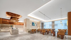 A modern hotel lobby with a marble floor, a central seating area with tables and chairs, and a kitchen area in the background.