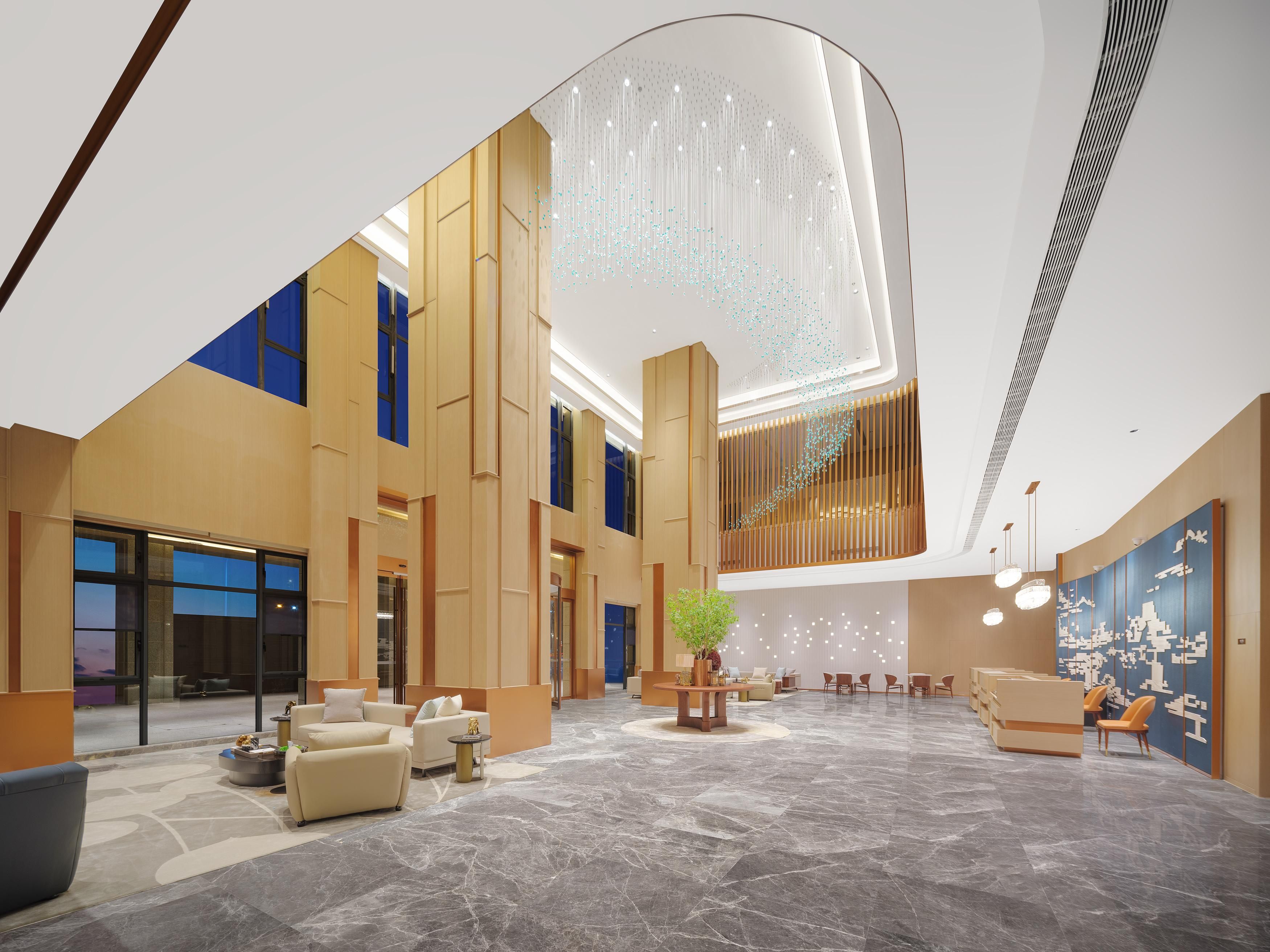 A spacious lobby with a high ceiling, marble flooring, and modern furnishings including sofas and a reception desk.