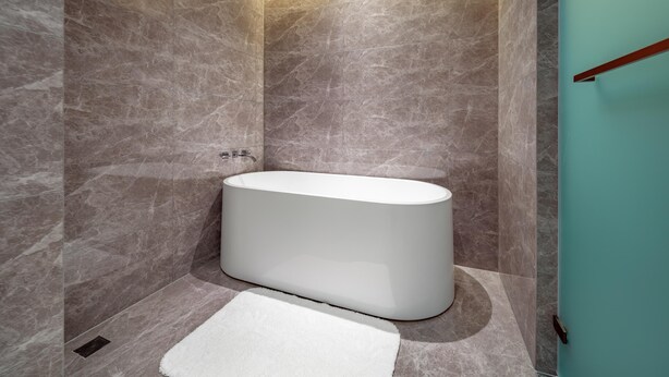A modern bathroom with a freestanding bathtub, marble walls, and a teal accent wall.