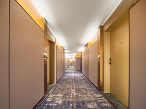 Un couloir d'hôtel avec des revêtements de sol en moquette, des portes en bois et des luminaires fixés au mur.
