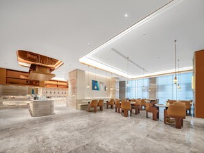 A modern hotel lobby with a marble floor, a central seating area with tables and chairs, and a kitchen area in the background. - Madison Hotel Wuxi Luocheng (Wuxi)