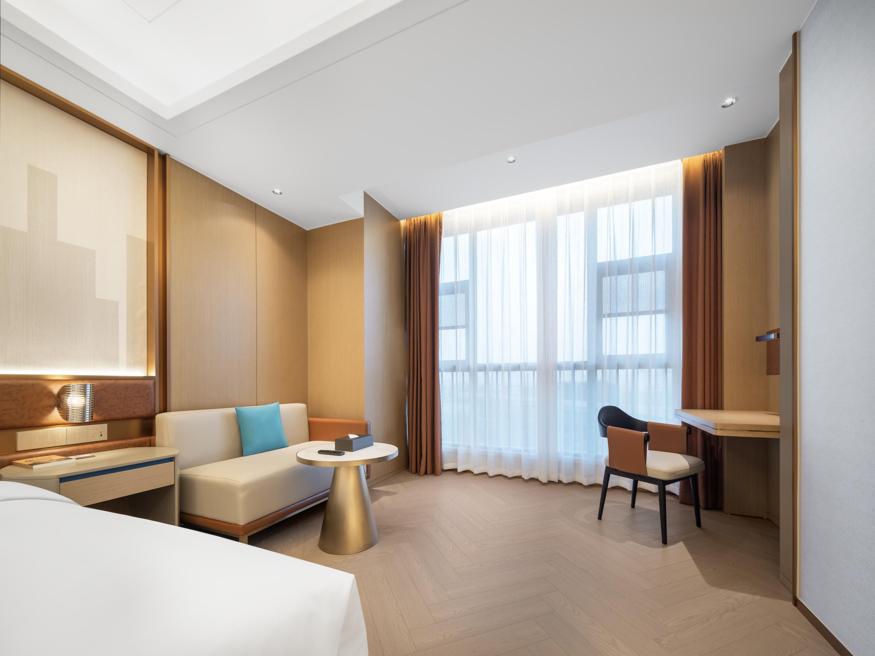 A modern hotel room with a bed, a sofa, a desk, and a chair.