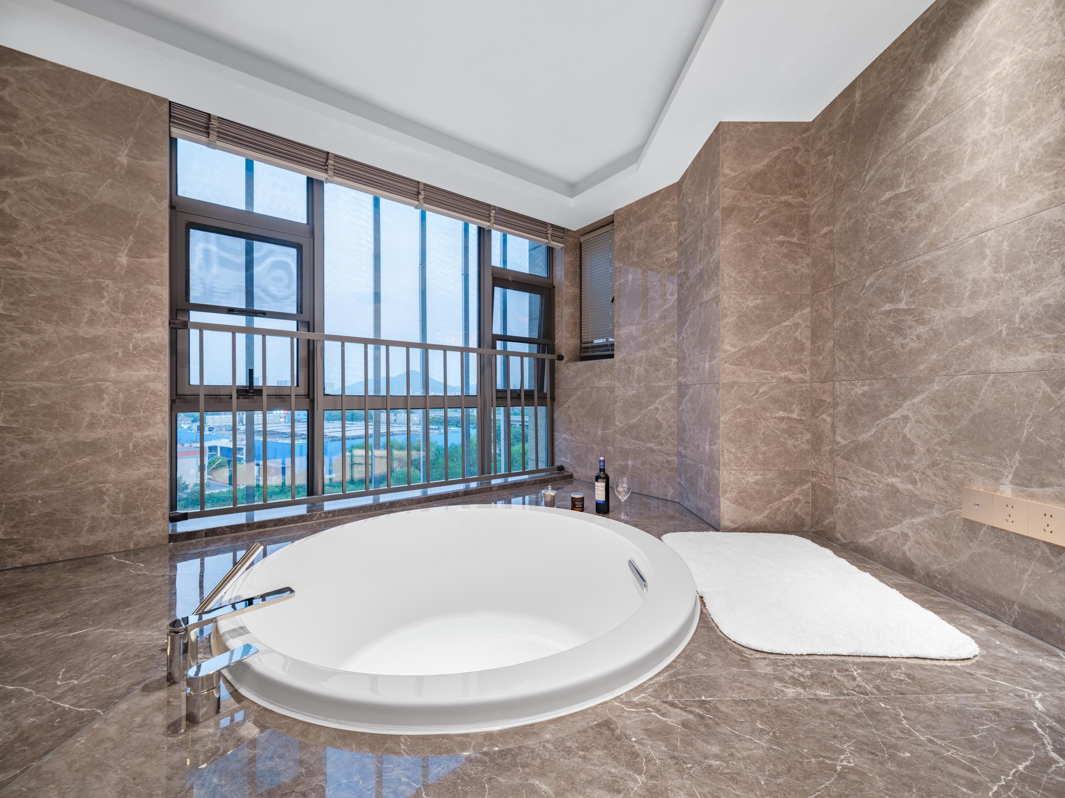 A modern bathroom with a large bathtub, a window with blinds, and a marble floor.