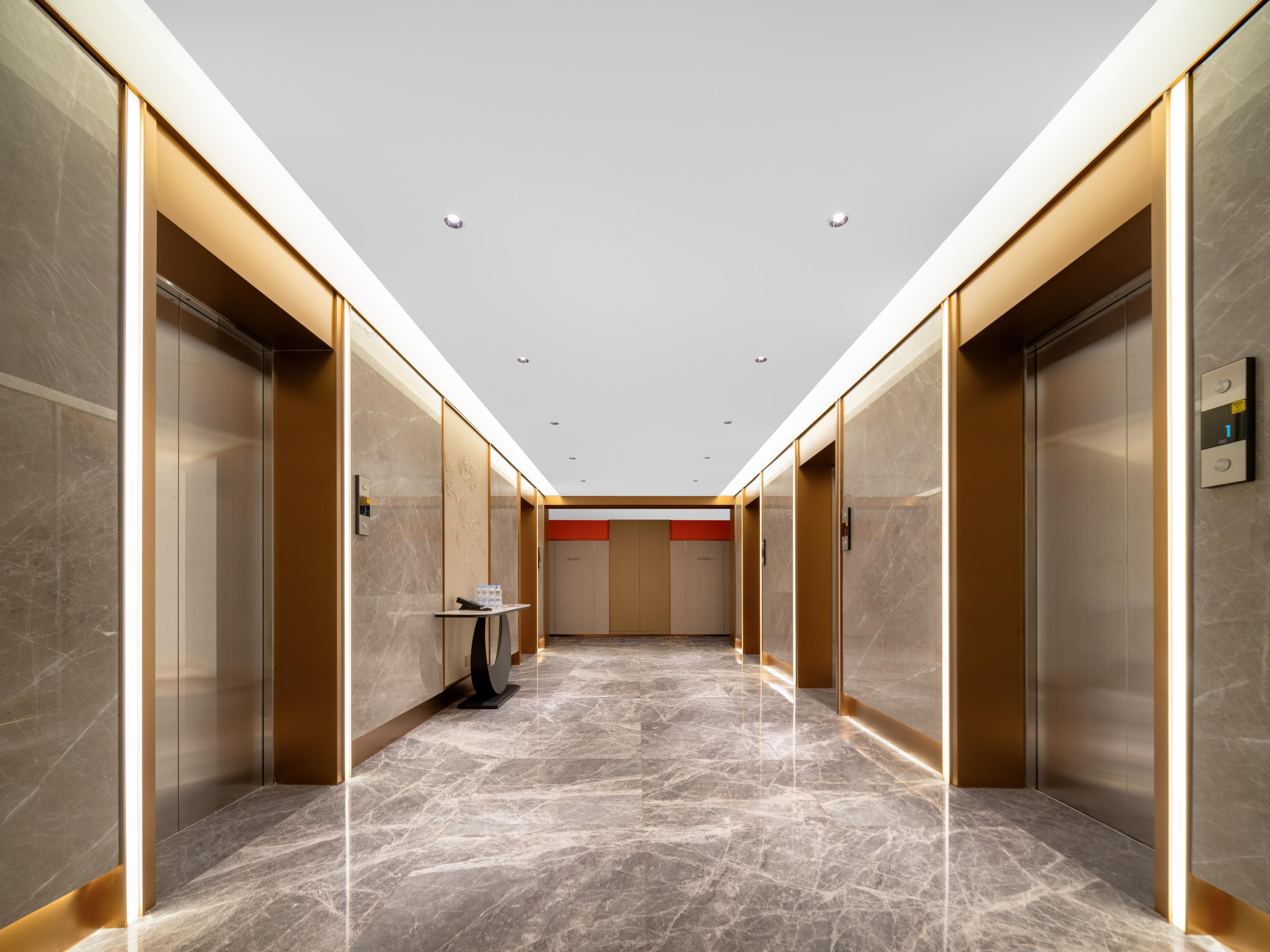 A modern elevator lobby with marble flooring, metallic elevator doors, and recessed lighting.