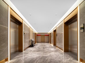 A modern elevator lobby with marble flooring, metallic elevator doors, and recessed lighting.
