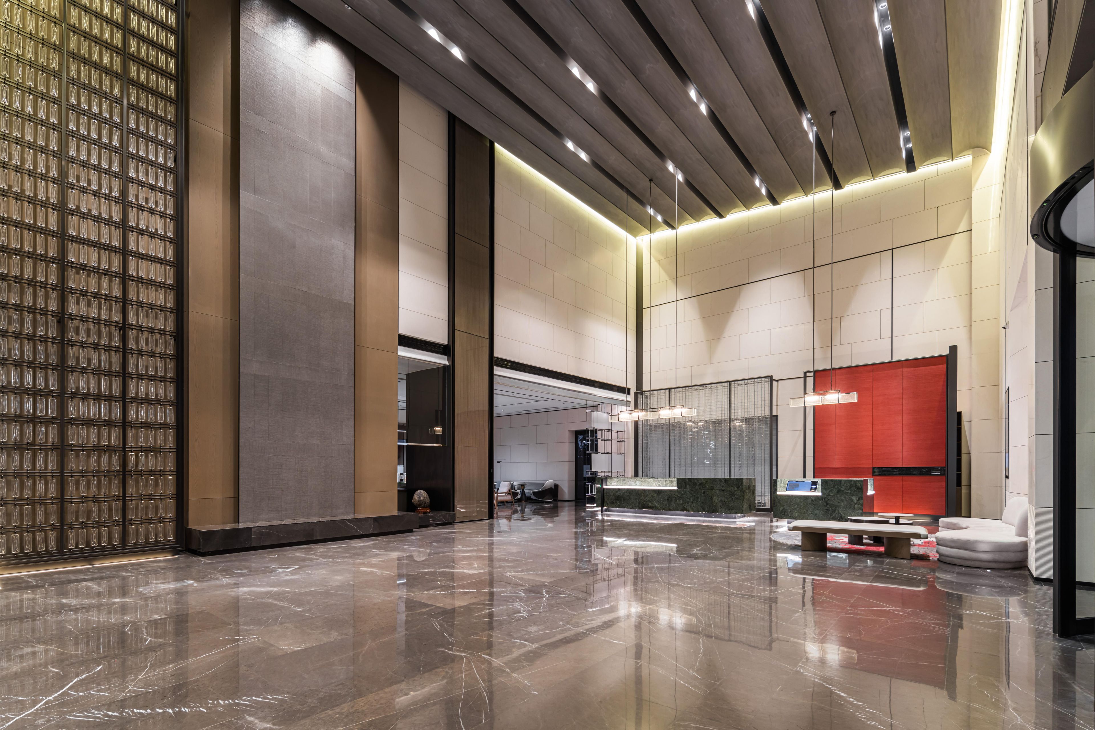 A spacious lobby with a polished marble floor, a seating area with a red accent wall, and a modern ceiling design.