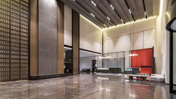 A spacious lobby with a polished marble floor, a seating area with a red accent wall, and a modern ceiling design.