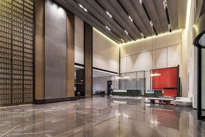 Un vestíbulo amplio con piso de mármol pulido, un área de descanso con pared de acento roja y un diseño de techo moderno.