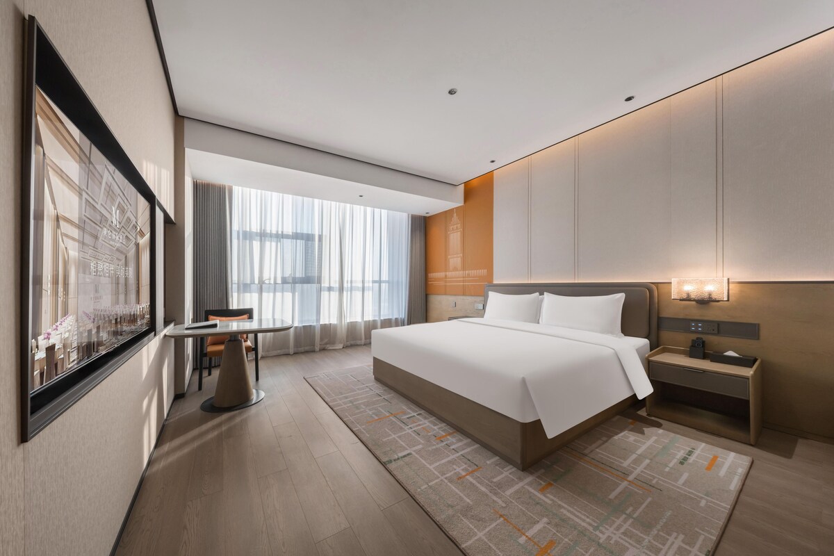 Una habitación de hotel moderna con una cama grande, un escritorio y vistas a la ciudad.