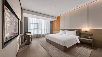 A modern hotel room with a large bed, a desk, and a view of the city.