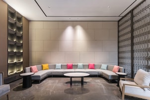 Un área de descanso moderna con un sofá curvo, mesas redondas y un revestimiento de pared con diseño.