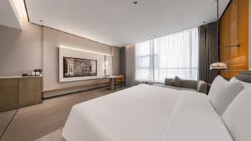 A modern hotel room with a large bed, a desk, a chair, and a large window with curtains.