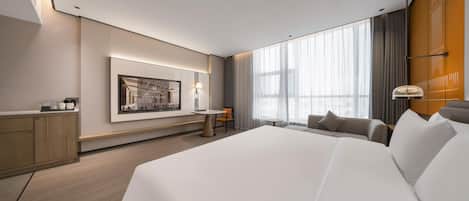 A modern hotel room with a large bed, a desk, a chair, and a large window with curtains.