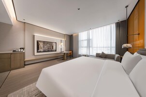 Una habitación de hotel moderna con una cama grande, un escritorio, una silla y un amplio ventanal con cortinas.