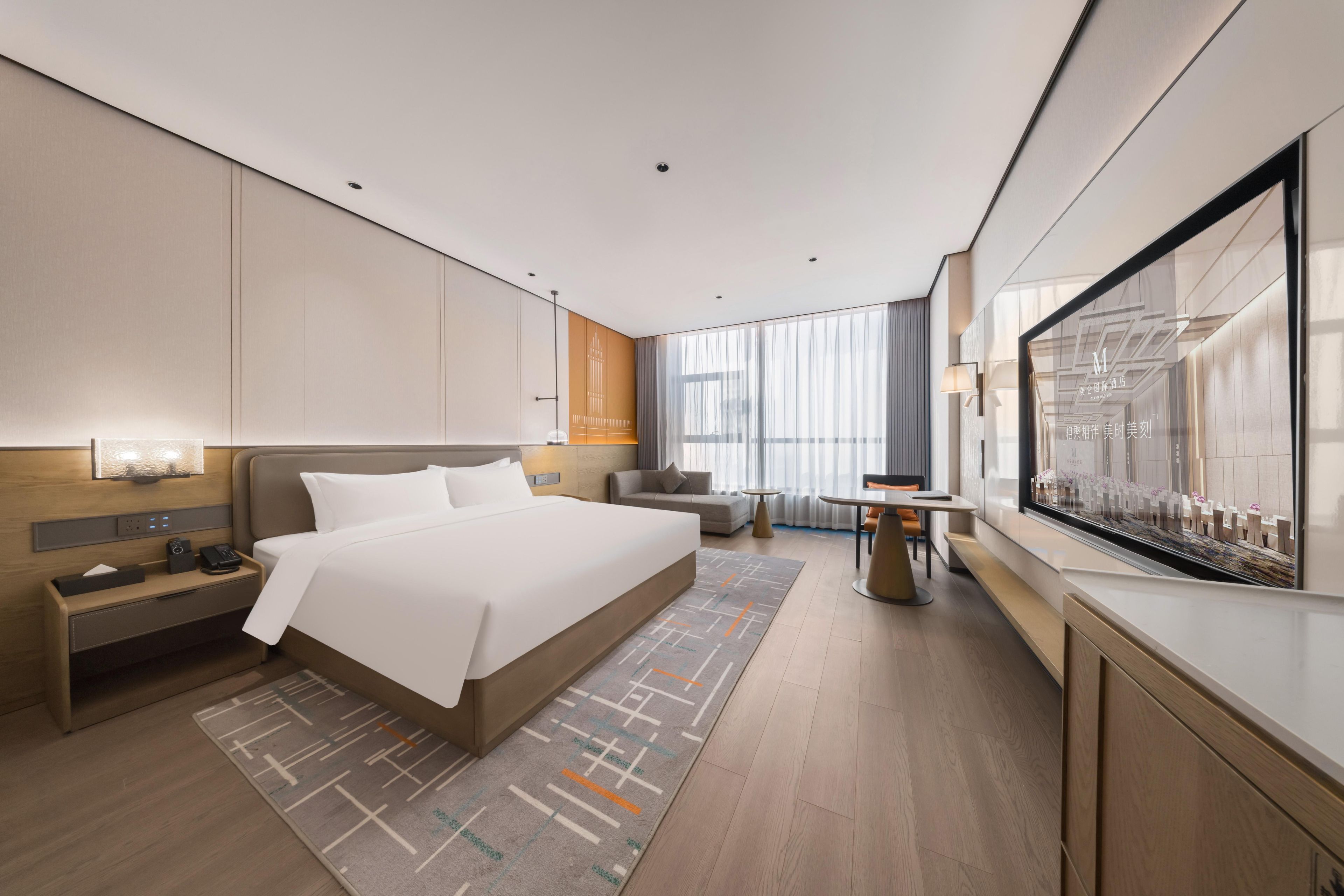 A modern hotel room with a large bed, bedside tables, a sofa, a small table, and a large window with curtains.