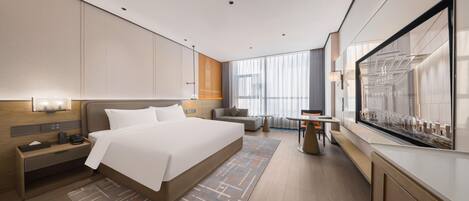 A modern hotel room with a large bed, bedside tables, a sofa, a small table, and a large window with curtains.