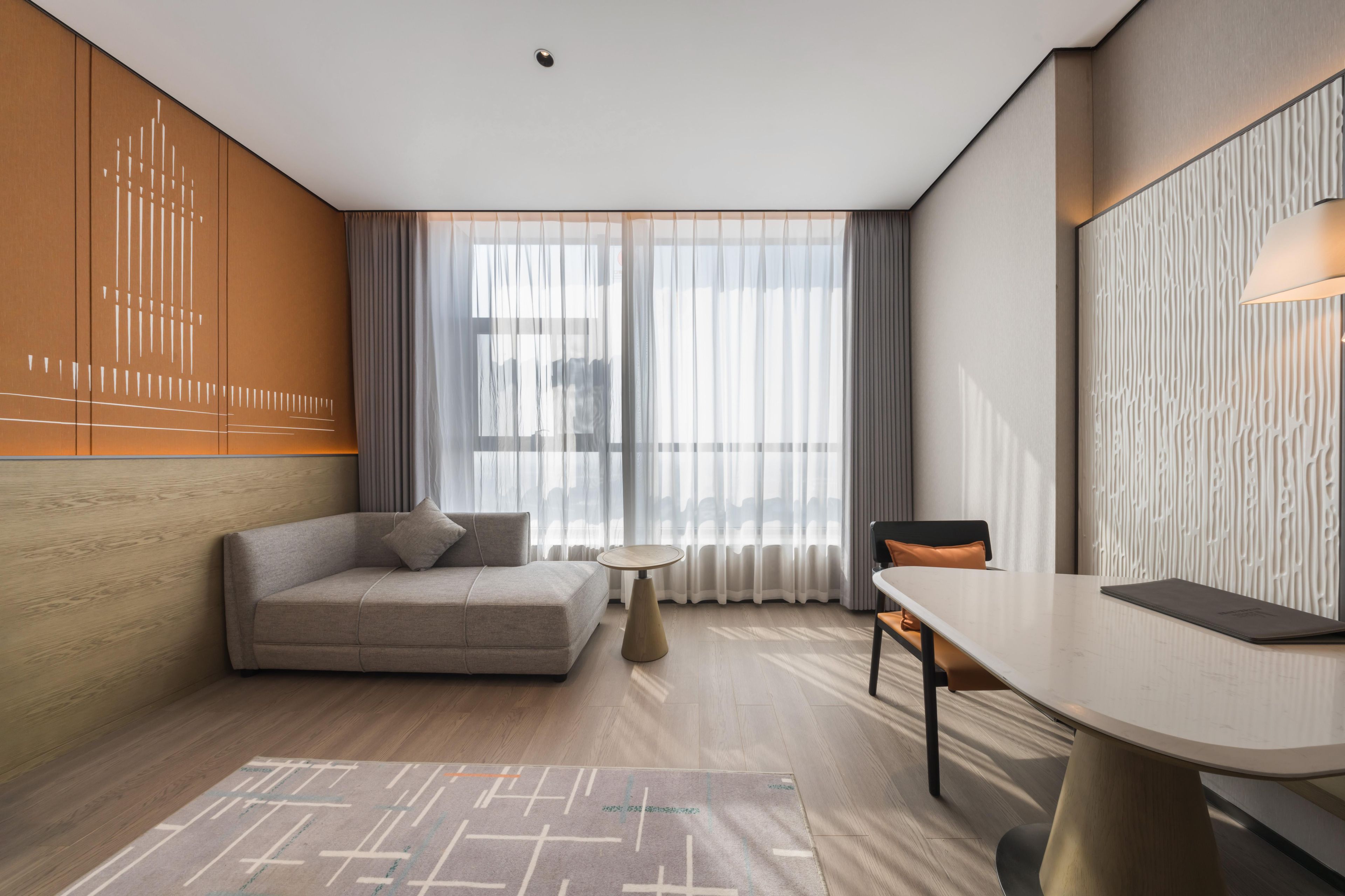 A modern hotel room with a sofa, a dining table, and a view through large windows.
