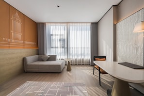 A modern hotel room with a sofa, a dining table, and a view through large windows. - Grand Madison Hotel Xiangyang Hexin Outlets (Xiangyang)