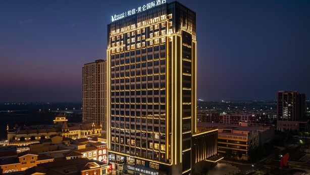 Um hotel moderno e alto, com letreiros iluminados, um pátio central e edifícios urbanos ao redor.