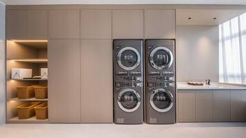 A modern laundry room with two wall-mounted washing machines, built-in shelving with baskets, and a large window providing natural light.