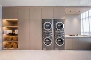 A modern laundry room with two wall-mounted washing machines, built-in shelving with baskets, and a large window providing natural light. - Grand Madison Hotel Xiangyang Hexin Outlets (Xiangyang)