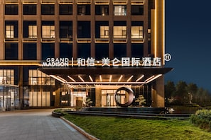 A hotel entrance with illuminated signage, a circular sculpture, and a landscaped garden area. - Grand Madison Hotel Xiangyang Hexin Outlets (Xiangyang)
