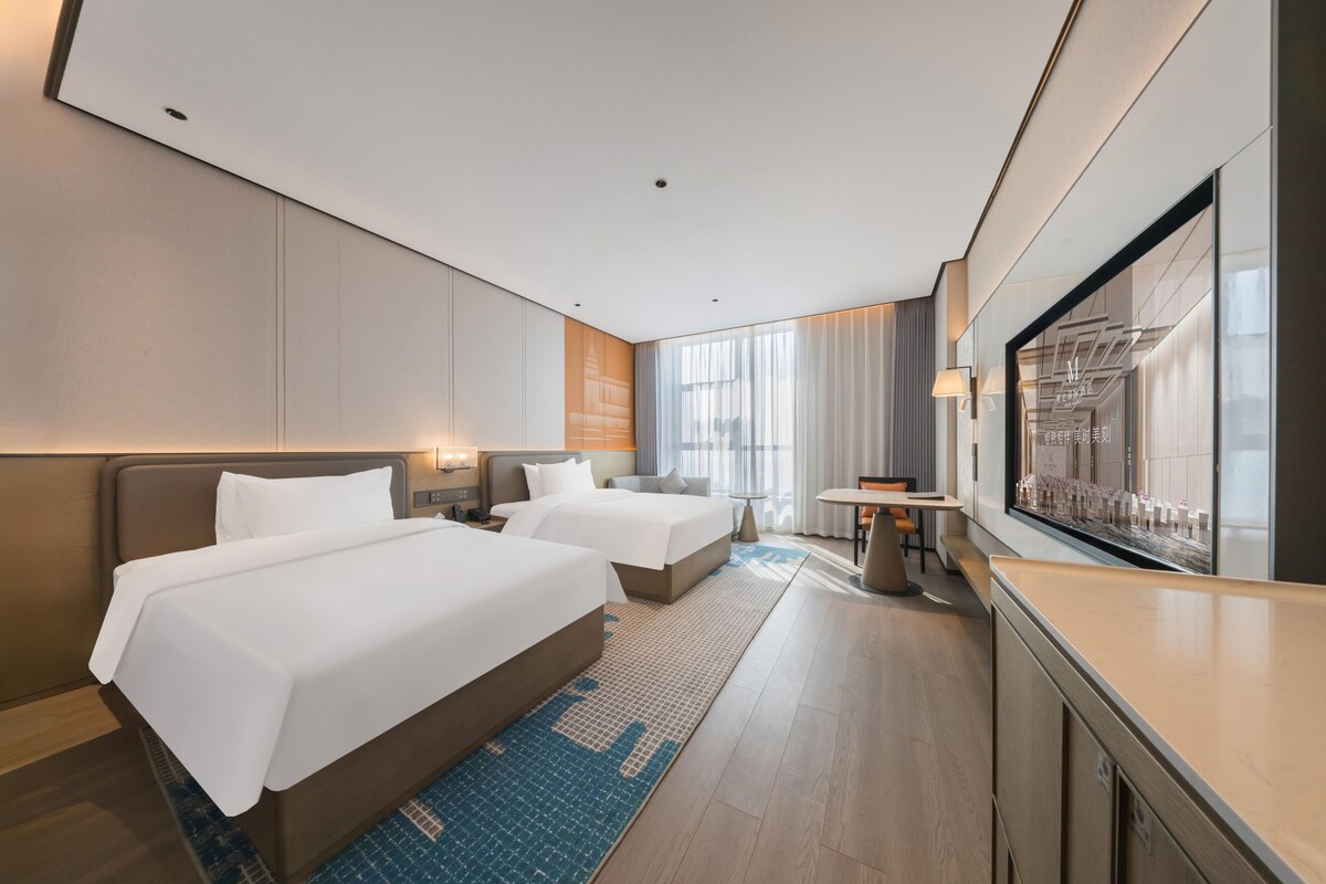 A modern hotel room with two beds, a desk, and a large TV.