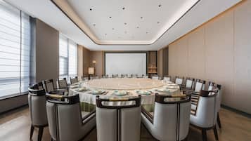 Un salón de conferencias con una mesa redonda, sillas y una pantalla grande.