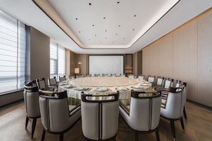 Un salón de conferencias con una mesa redonda, sillas y una pantalla grande.