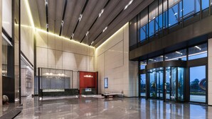 Um hall amplo com piso de mármore, balcão de recepção, parede com detalhes em vermelho e um elevador de vidro.