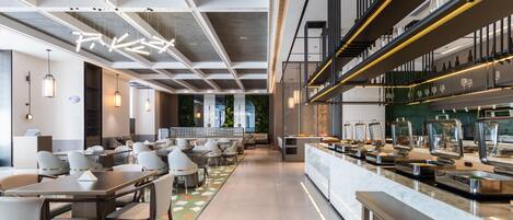 A modern restaurant with a long counter, multiple seating areas, and a high ceiling with exposed beams.