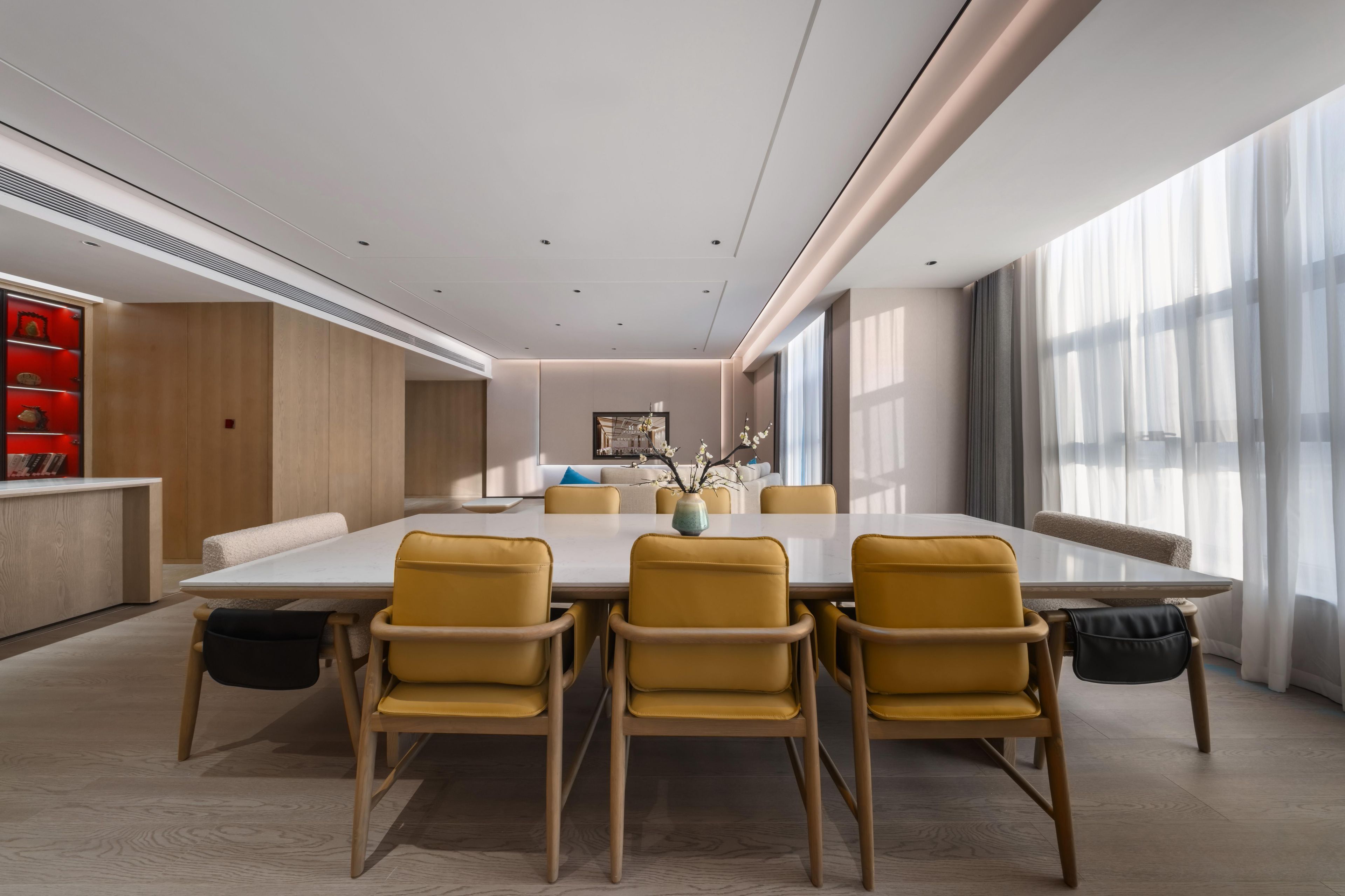 Un comedor moderno con una mesa grande y sillas amarillas, un armario de madera y vistas a la ciudad a través de ventanas amplias.