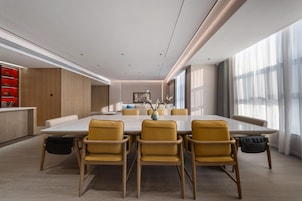 Un comedor moderno con una mesa grande y sillas amarillas, un armario de madera y vistas a la ciudad a través de ventanas amplias.