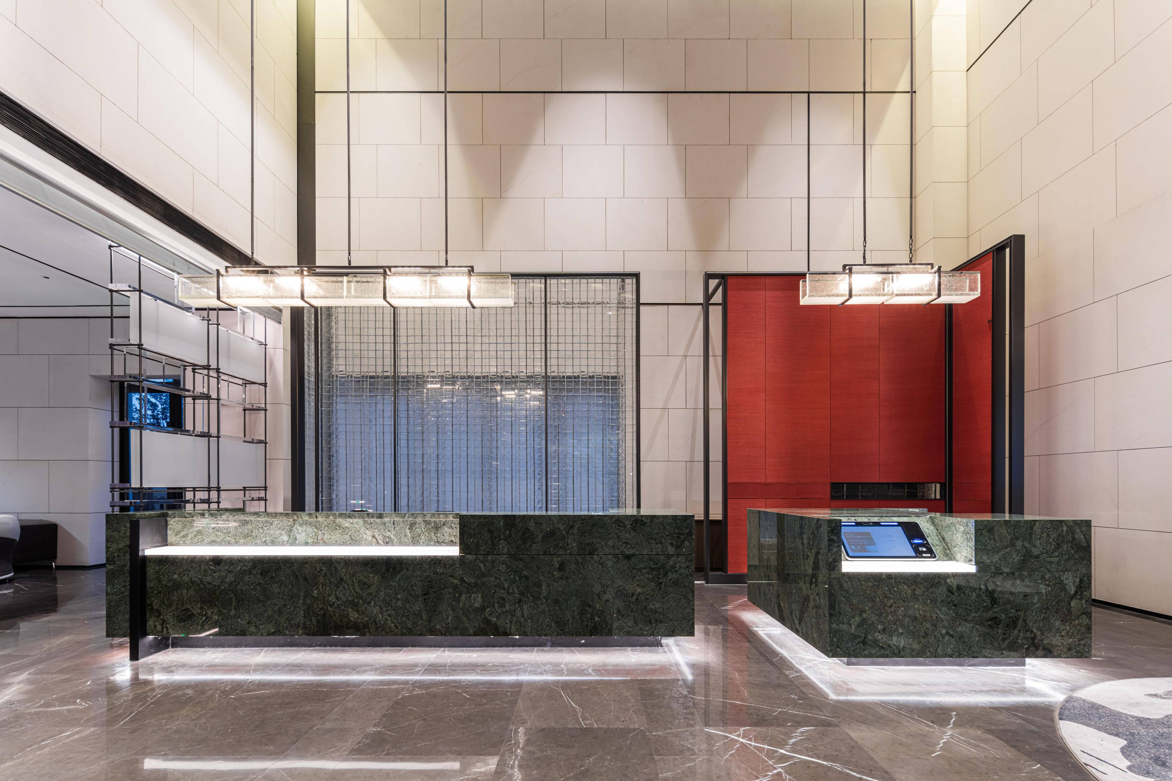 Un vestíbul modern amb taulells de recepció de marbre, una gran separació de vidre i una paret decorativa vermella.