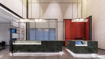 Eine moderne Lobby mit Marmor-Rezeptionstheken, einer großen Glasscheibe und einer roten Akzentwand.