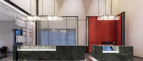 Un vestíbulo moderno con mostradores de recepción de mármol, un amplio separador de vidrio y una pared decorativa roja.