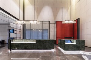 Un vestíbulo moderno con mostradores de recepción de mármol, un amplio separador de vidrio y una pared decorativa roja.