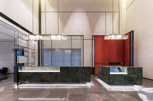 Un vestíbulo moderno con mostradores de recepción de mármol, un amplio separador de vidrio y una pared decorativa roja.