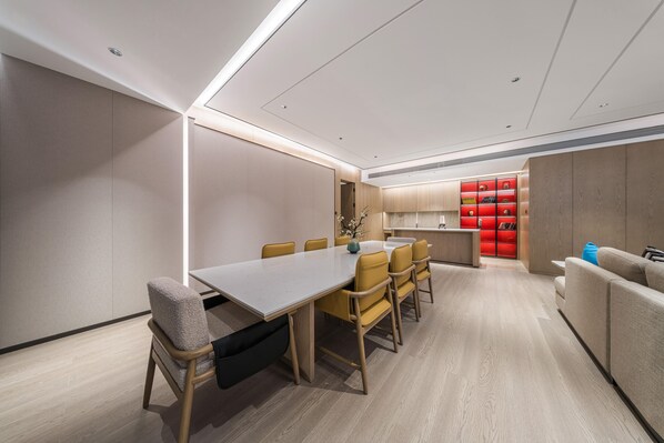Un espace repas moderne avec une longue table et des chaises, une cuisine en arrière-plan et un meuble de rangement rouge.